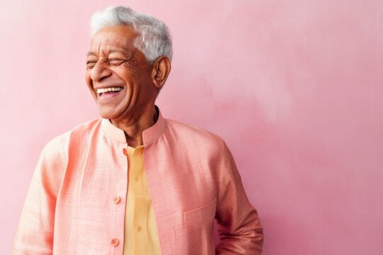 Lifestyle portrait of an Indian man in his 70s against a pastel or soft colors background wearing a cardigan