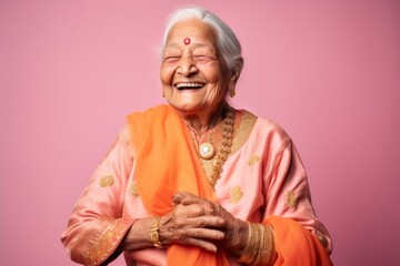 Fototapeta premium Portrait of a happy senior woman in traditional indian clothing posing against pink background
