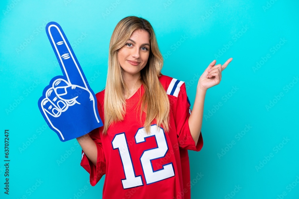 Wall mural uruguayan sports fan woman isolated on blue background pointing finger to the side