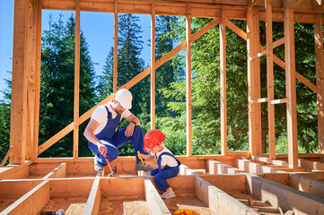 Father with toddler son building wooden frame house. Male worker instructing his son on practice of utilizing hammer to secure nails on construction site. Carpentry and family concept.