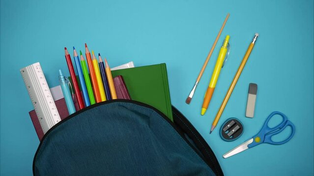 Stop motion animation of colorful school supplies moving from school bag on blue background. Back to school concept. Top view