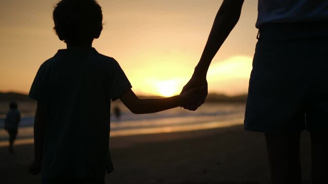 Experience the heartwarming essence of family connection as the silhouette of a mother and her son is beautifully captured against the backdrop of a mesmerizing sunset on a tranquil beach. T