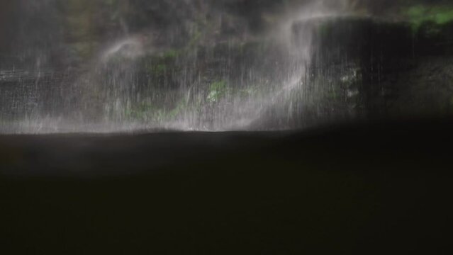 First-person view. The water in the reservoir rises at eye level, water falls from the mountain. A man is hiding in the water, spying.