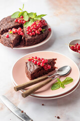 A piece of chocolate cake brownie decorated with red currant berries and mint on white marble table