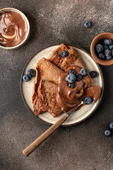 Chocolate crepes with blueberry and chocolate paste on brown textured background rustic style top view, flat lay