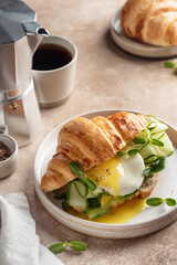 Croissant sandwich with fried egg, cheese, cucumber and micro greens and coffee over beige...