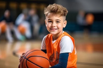 Fotobehang Portrait of smiling little boy with basketball ball looking at camera in gym © igolaizola