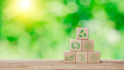 Hand holding wooden cube block put stack on wood table with recycle, earth, eco friendly and green energy icon in green background. Sustainable and environmental responsibility concept.