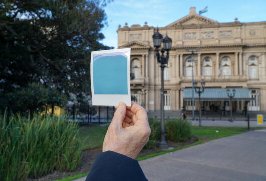 A person holding a polaroid picture in front of the Colon theater in Buenos aires, Argentina.