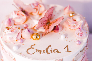 Birthday cake decorated with pink sugar flowers and butterflies, Emilia name is written on it.