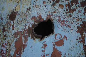 one rusty ragged hole in metal from bullet on black background. blue and brown painted wall with gap. - obrazy, fototapety, plakaty
