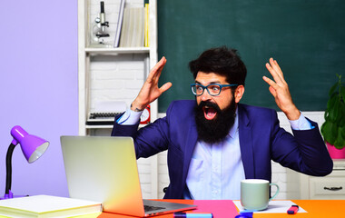 Excited male student with raised hands at classroom. Success. Happy student in university campus. Happy teacher man working with laptop. Exam in college. Schooling, education. E-learning. Online test.