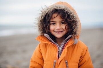 Medium shot portrait of an Indian child female wearing a warm parka in a beach 