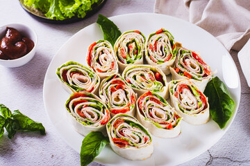 Rolled up sandwiches with lettuce, bacon and baked peppers in a tortilla on a plate