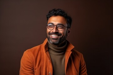 Fototapeta premium Portrait of a smiling Indian young man in orange coat and glasses