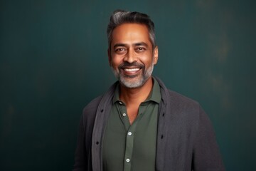 Obraz premium Portrait of a handsome Indian man smiling at the camera against a green background