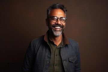 Obraz premium Portrait of a smiling indian man wearing glasses against brown background