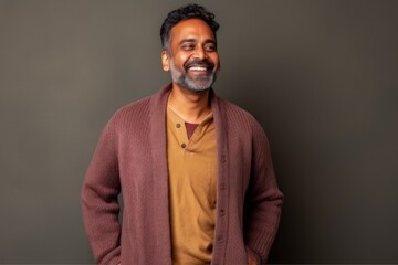 Obraz premium indian man with beard and brown sweater on grey background smiling at camera
