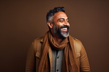 Fototapeta premium Portrait of a smiling indian man wearing scarf and coat against brown background