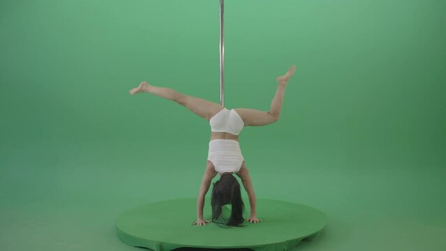 Woman holding inverted position on pole with legs spread on green screen, advanced pole sport chroma key footage