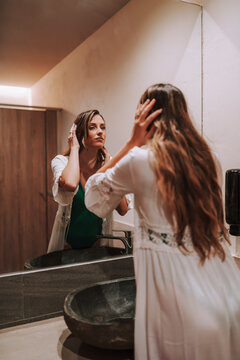 Chica joven en cuarto de baño frente a espejo retocándose el pelo y haciéndose fotos con el smartphone