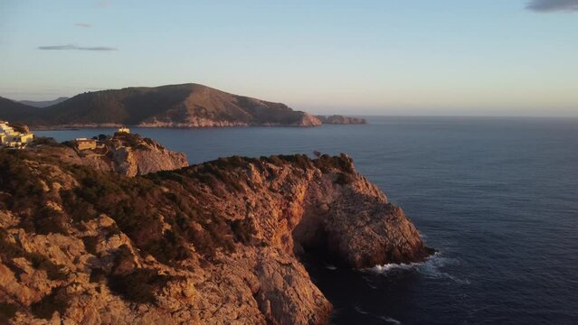 Drone scene over Far de Capdepera lighthouse in Spain with golden sunset sky