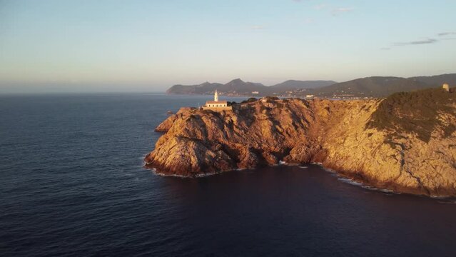 Drone footage over Far de Capdepera lighthouse on rocky cliff in Spain with  sunset sky