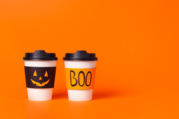 Two halloween coffee cups with jack-o-lantern face and word boo on orange background.