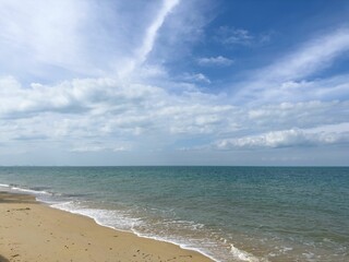 Scenic beach landscape with a sandy shoreline and white clouds in the sky.