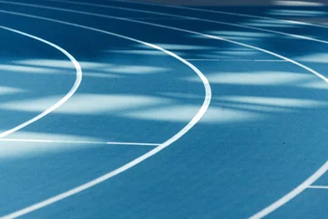 Fotobehang Blue running track with crisp white lines. © Eyesightpics/Wirestock Creators