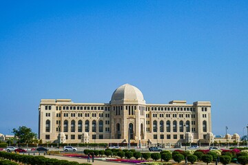 View of the Supreme Court of Oman against a bright blue sky and lush, green gardens - obrazy, fototapety, plakaty