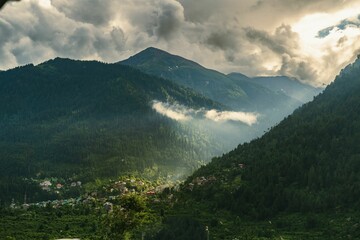 Obraz premium a cloudy sky over mountains with cows grazing on the side