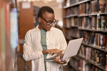 Busy African Black girl student wearing eyeglasses using laptop standing in university or college...