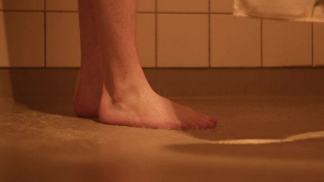Soapy water drains into the floor drain as the man showers. Only his feet are visible.