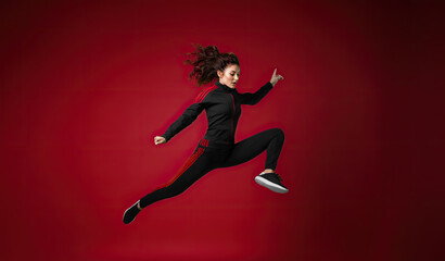 Fototapeta na wymiar A trendy and athletic dancer jumps on a trampoline in a red studio