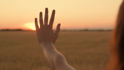 Happy girl stretches her hand to yellow sunset. Sun between fingers of girls hands. Teenager girl...