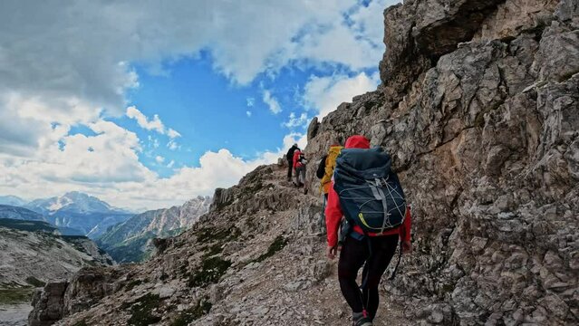 Active people with backpacks hiking narrow pathway and climbing Tre Cime di Lavaredo Dolomites mountain. Group of friends summer adventure journey in nature. Travel exploring Alps, Dolomites, Italy