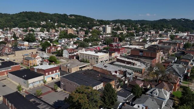 A slow forward aerial establishing shot view of a small Pennsylvania town. Church and apartment building in the distance, main street businesses below. Pittsburgh suburbs.  	