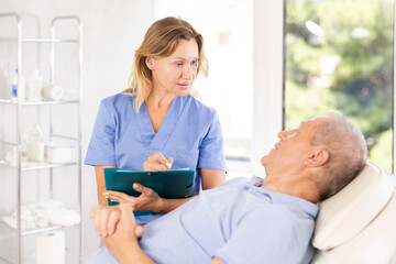 Obraz premium Retired man is sitting in chair at clinic reception and carefully answers doctor questions about his well-being, health complaints