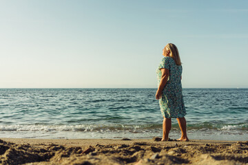 beautiful grandmother blonde in a dress walks on the sand on the beach near the sea vacation pension travel