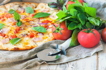 A fragment of Italian pizza,basil leaves and vegetables on a background of linen fabric, selective focus.	
