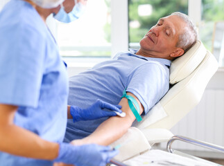 Obraz premium Adult woman doctor in medical uniform makes injection in arm of elderly man in medical office