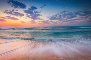 Color tropical ocean sunrise with scenic cloudscape over the sea waves and beach shore
