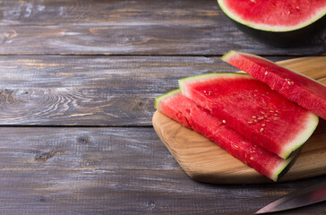 Seedless watermelon, slices on a wooden board with a knife and half of a watermelon on a wooden background