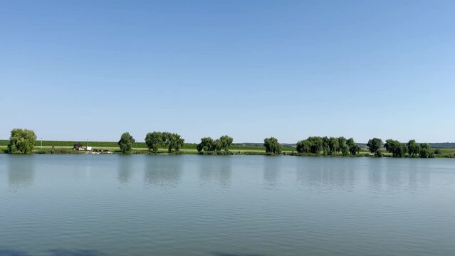A view of a beautiful large lake on a sunny day against the background of a blue clear sky, on the shore of which people with tents among green trees are resting and fishing in summer. Rest and fishin