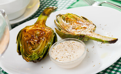 Delicious roasted halves of artichoke served with sea salt and sauce. Healthy vegetarian food..