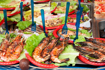 Street food at the market in Catania, Sicily island, Italy. Grilled shrimp served on a red plate...