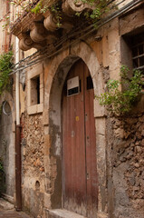 Fototapeta na wymiar Old wooden door in a stone wall.Narrow street of the old city.Syracuse,Italy.