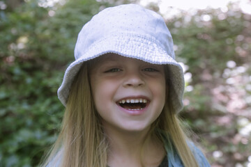 Candid headshot of adorable little girl wearing bucket hat in the forest, spending time in the nature, outdoors experience in the countryside