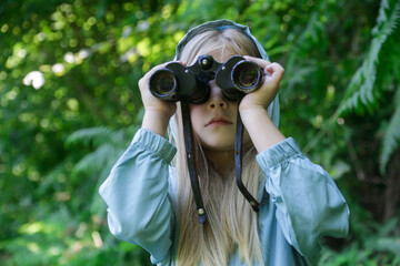 Cute little girl exploring nature looking through binoculars. Child playing outdoors. Kids travel, adventure and bird watching concept.